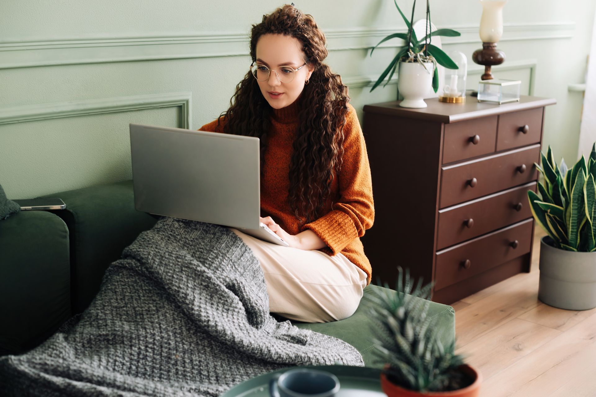 A woman is sitting on a couch using a laptop computer.
