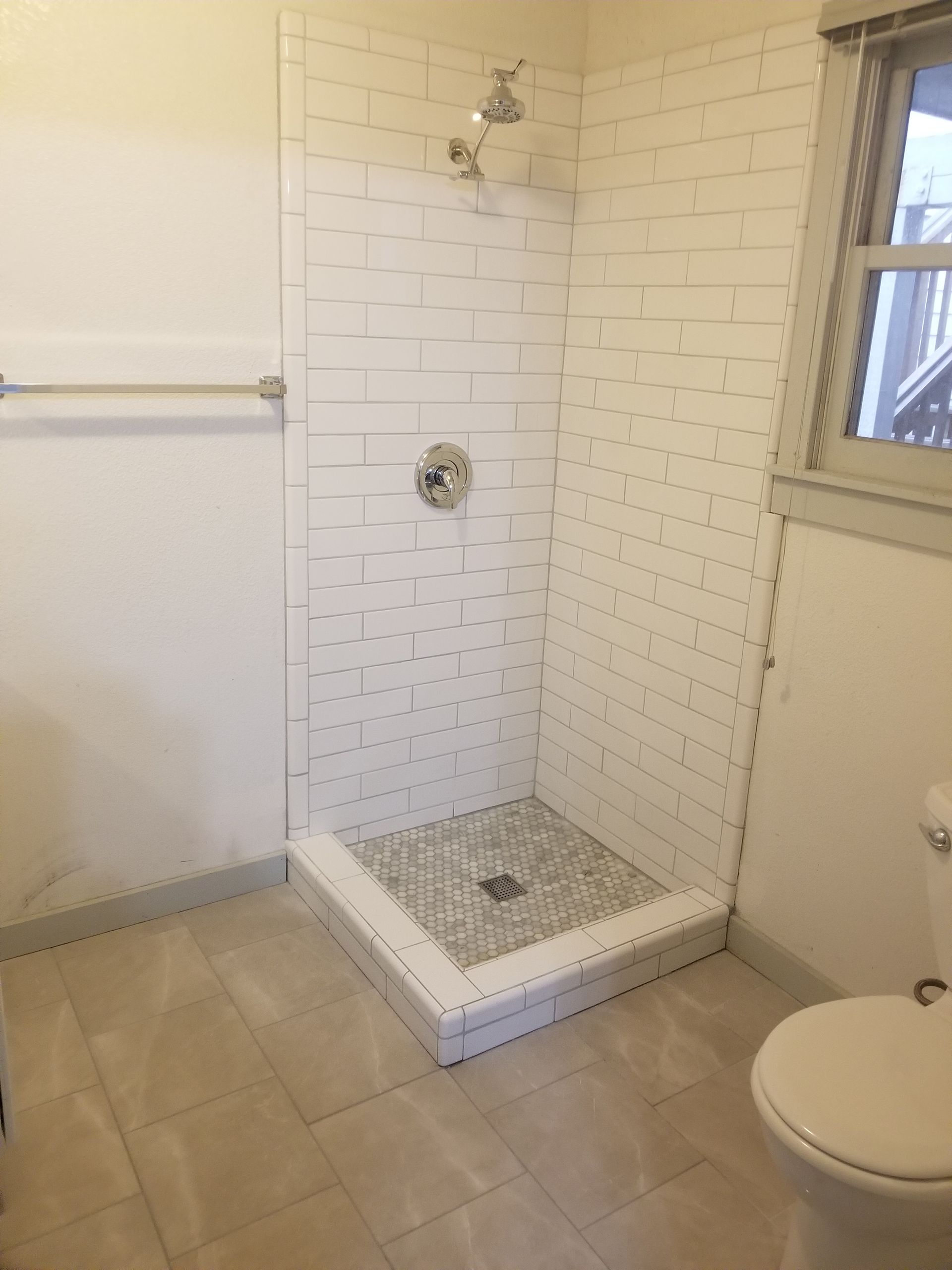 Bathroom with white tile shower, gray floor, and a toilet.