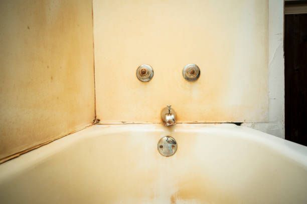 Bathtub with rust stains, three faucet knobs forming a face on the wall.