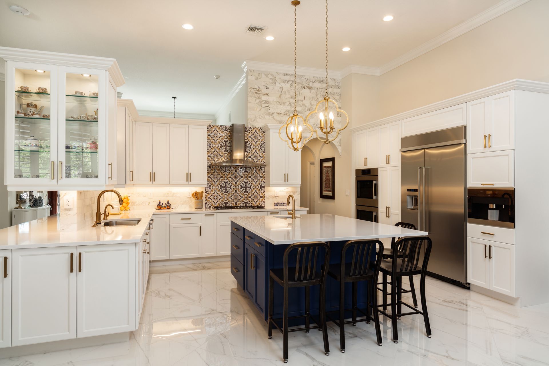 Spacious white kitchen with blue island and gold pendant lights. Stainless steel appliances.