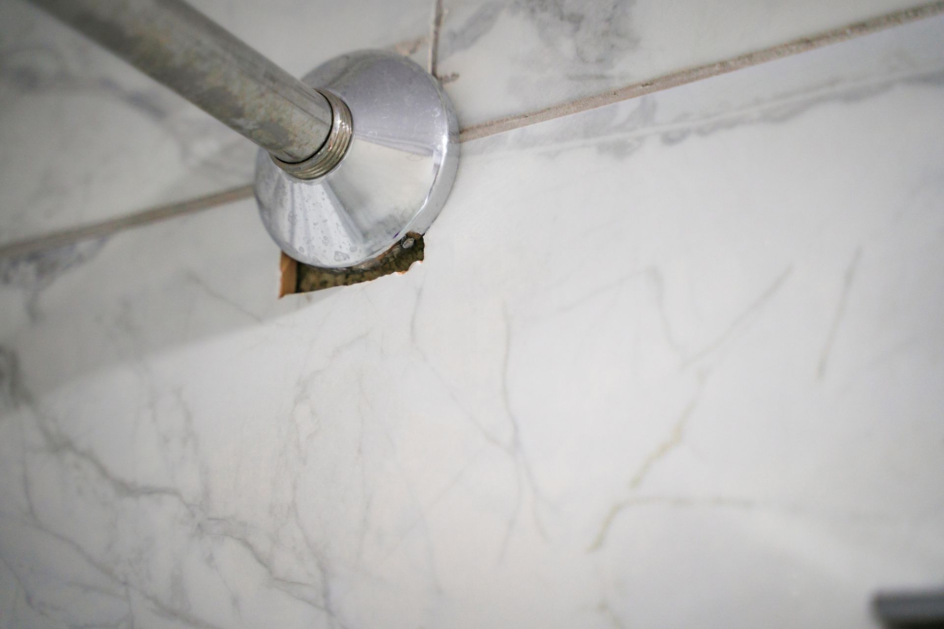 Chrome shower rod with a broken tile, revealing the wall behind it.