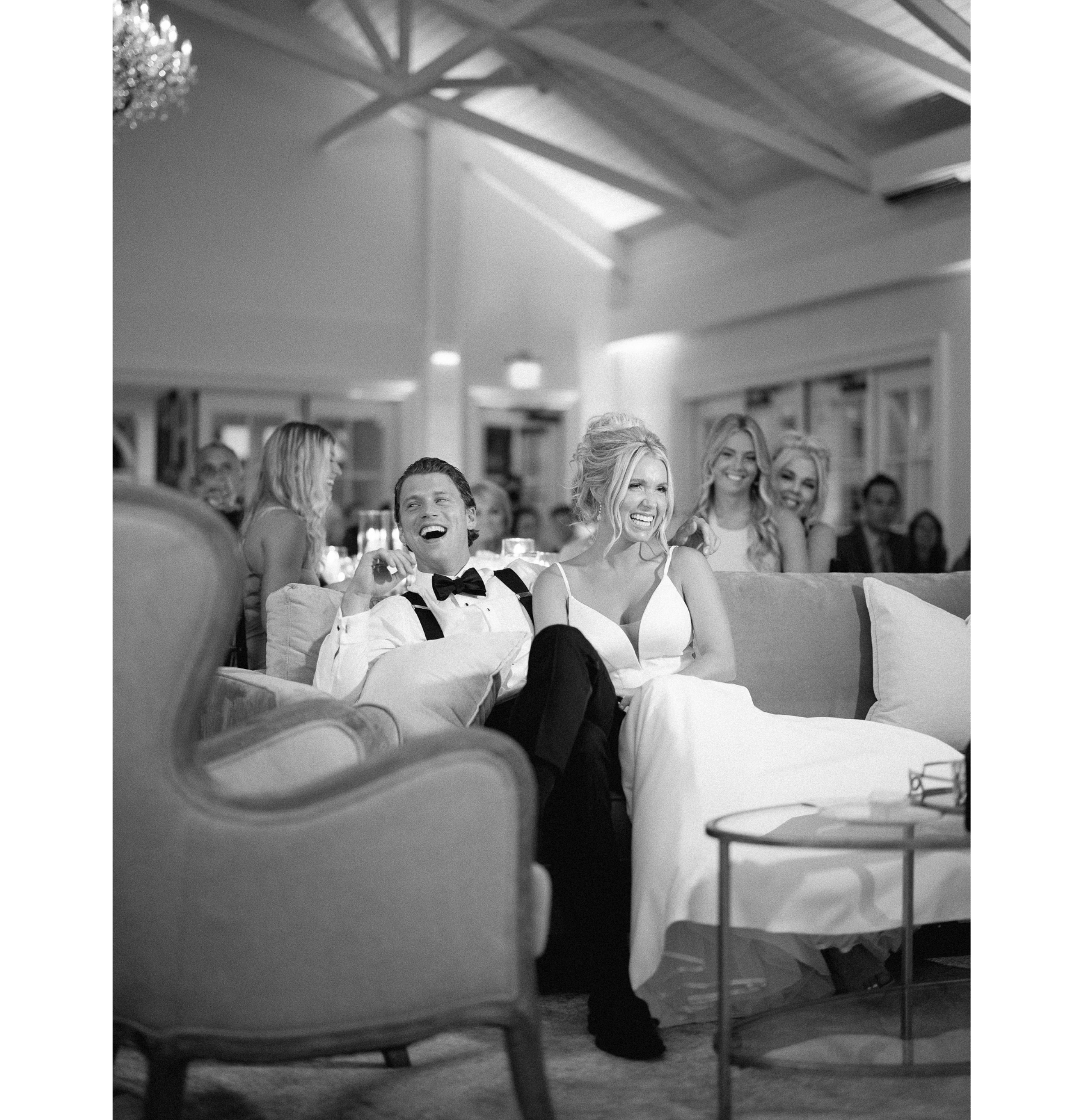 A black and white photo of a bride and groom sitting on a couch enjoying wedding toasts.