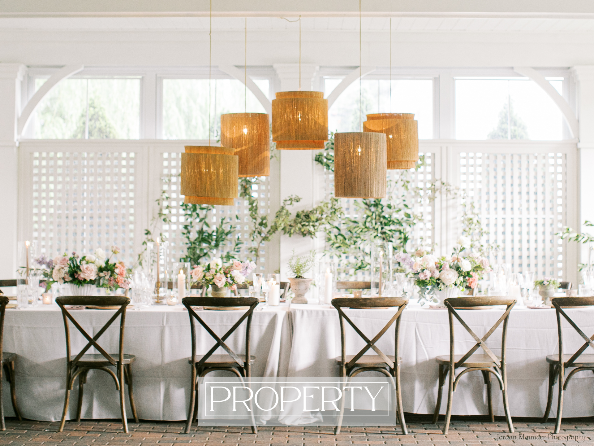 A long dinner table with rattan chandeliers hanging above and wood chairs set around the table. 