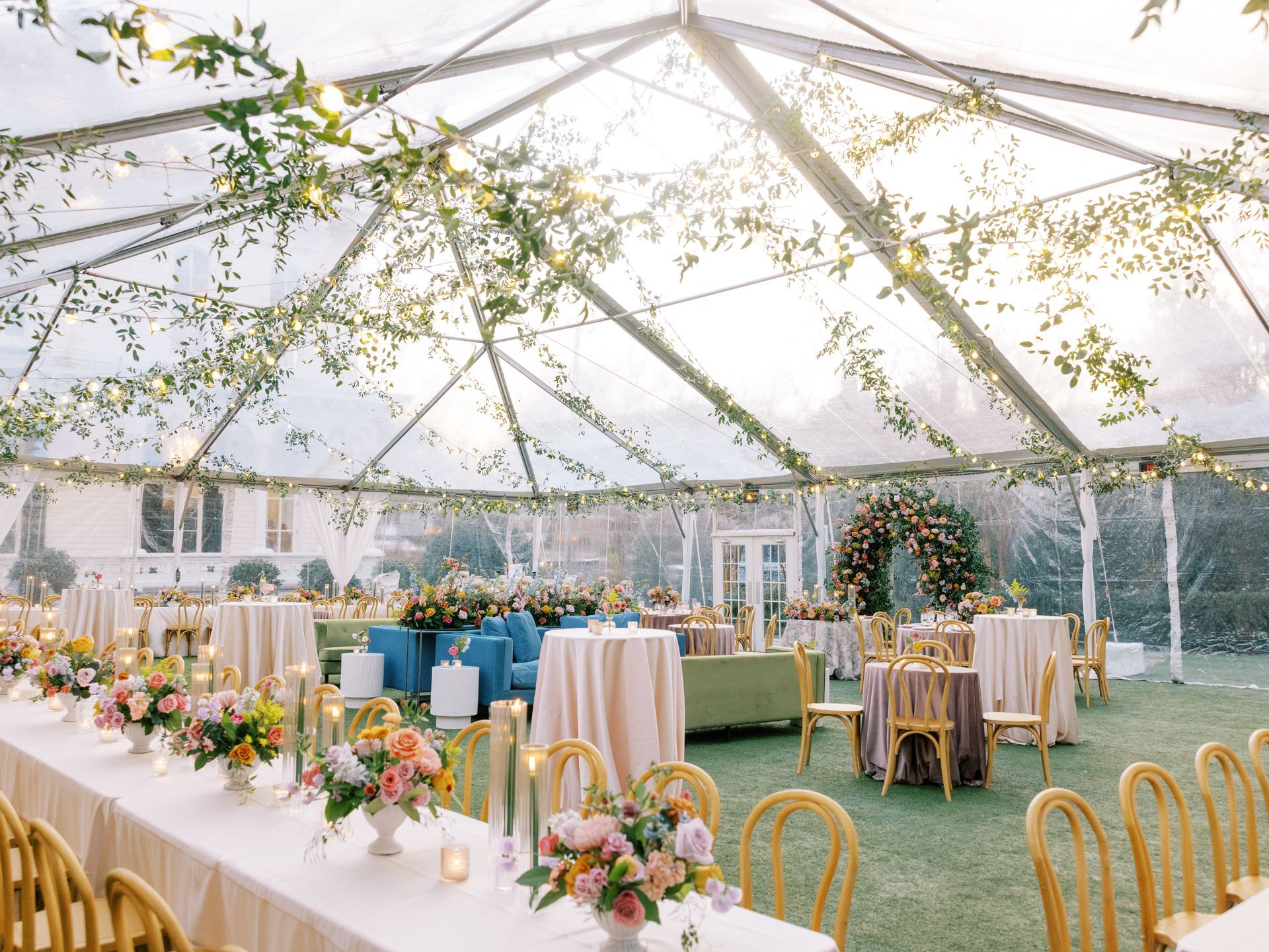 A bride and escort walk across a sunny lawn toward guests seated under white umbrellas at an outdoor wedding ceremony.