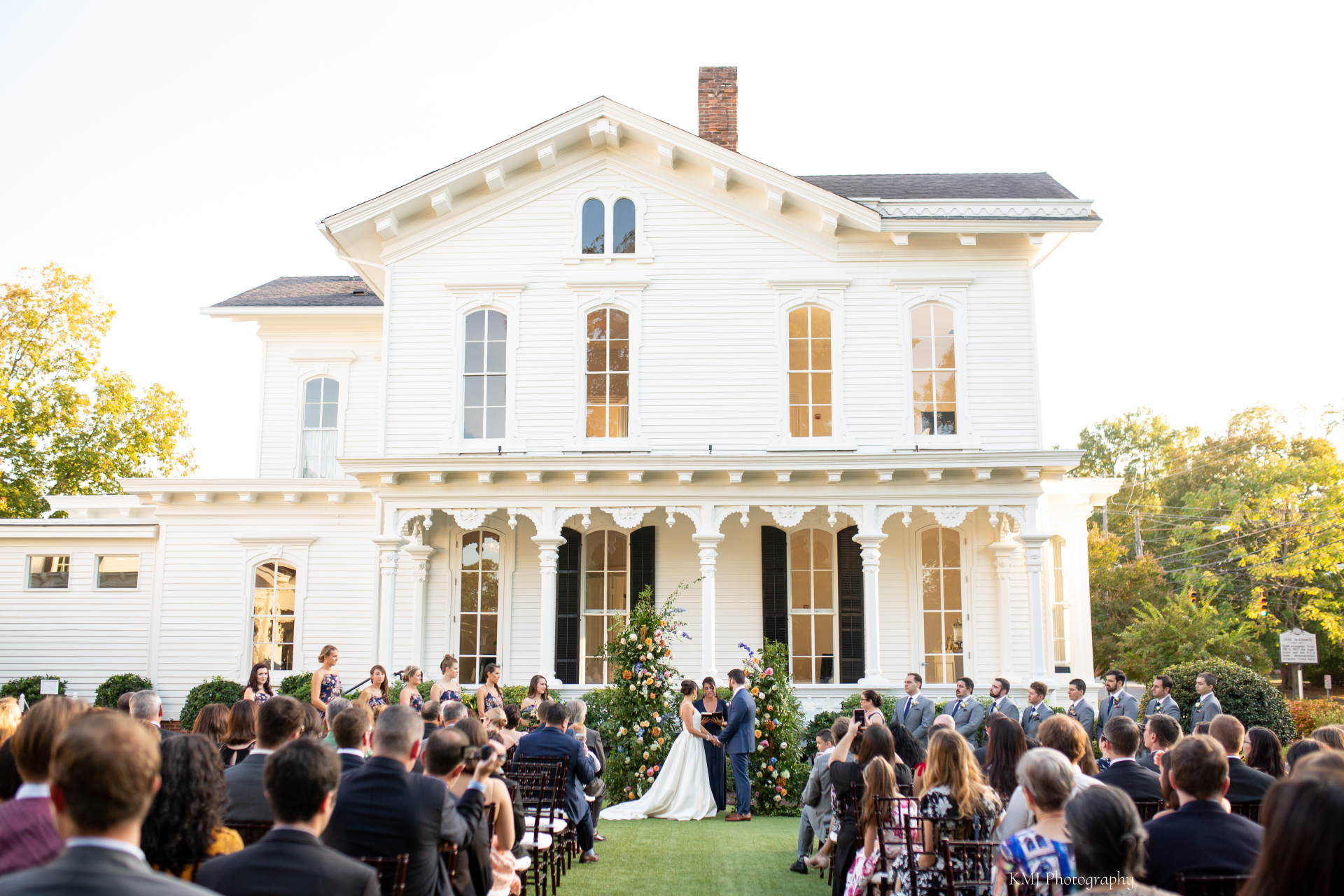 A bride and groom are getting married in front of a large white house.