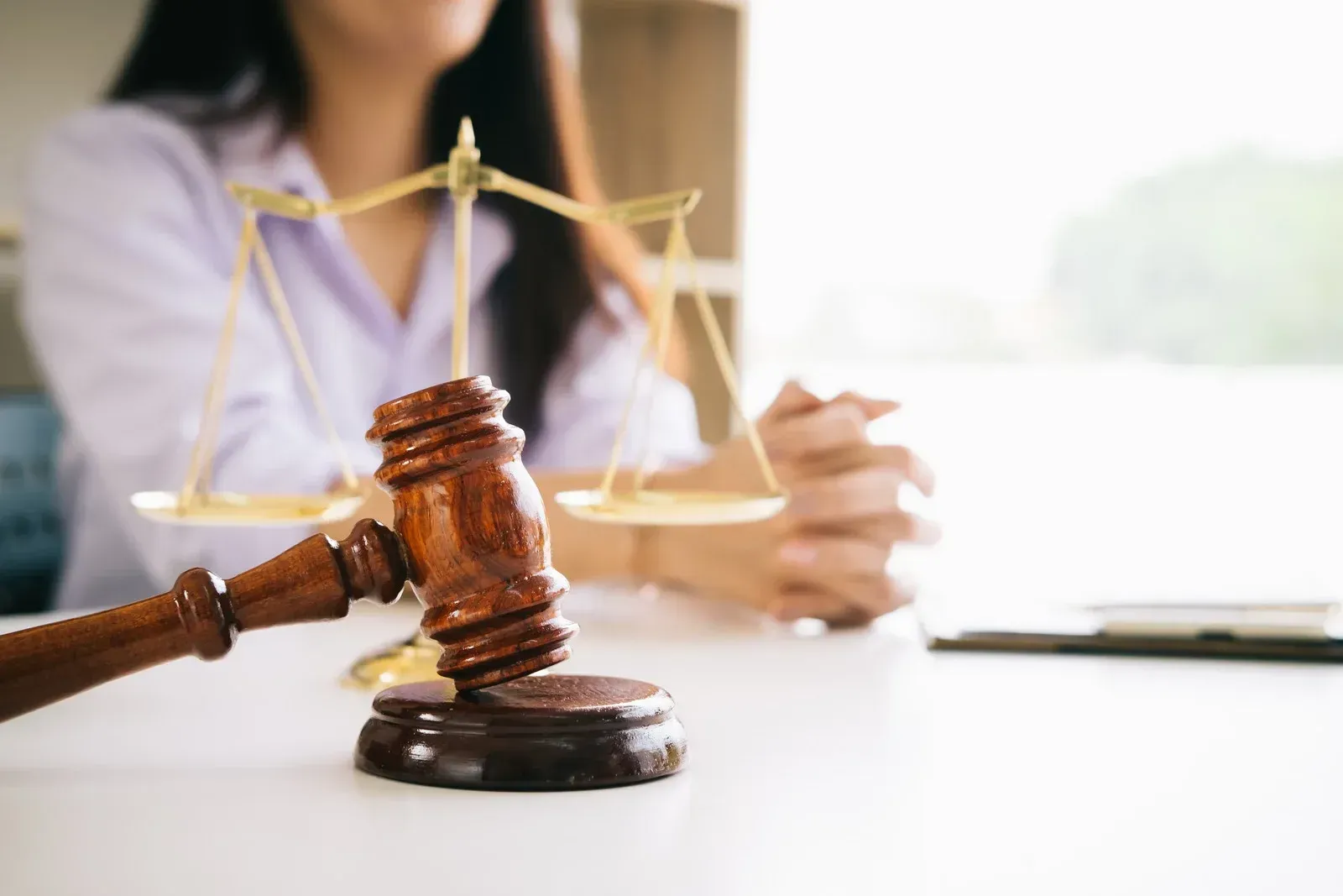 A woman is sitting at a table with a wooden gavel and scales of justice.