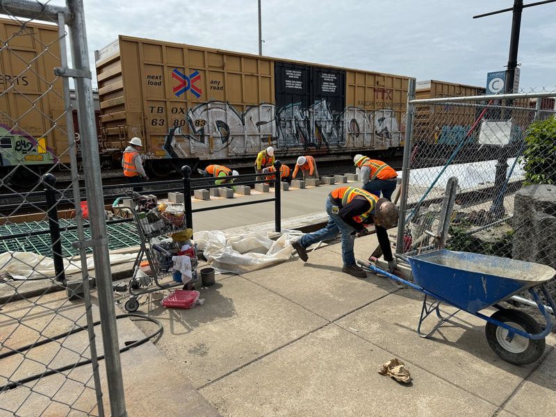 A group of construction workers are working on a sidewalk in front of a train car with graffiti on it.