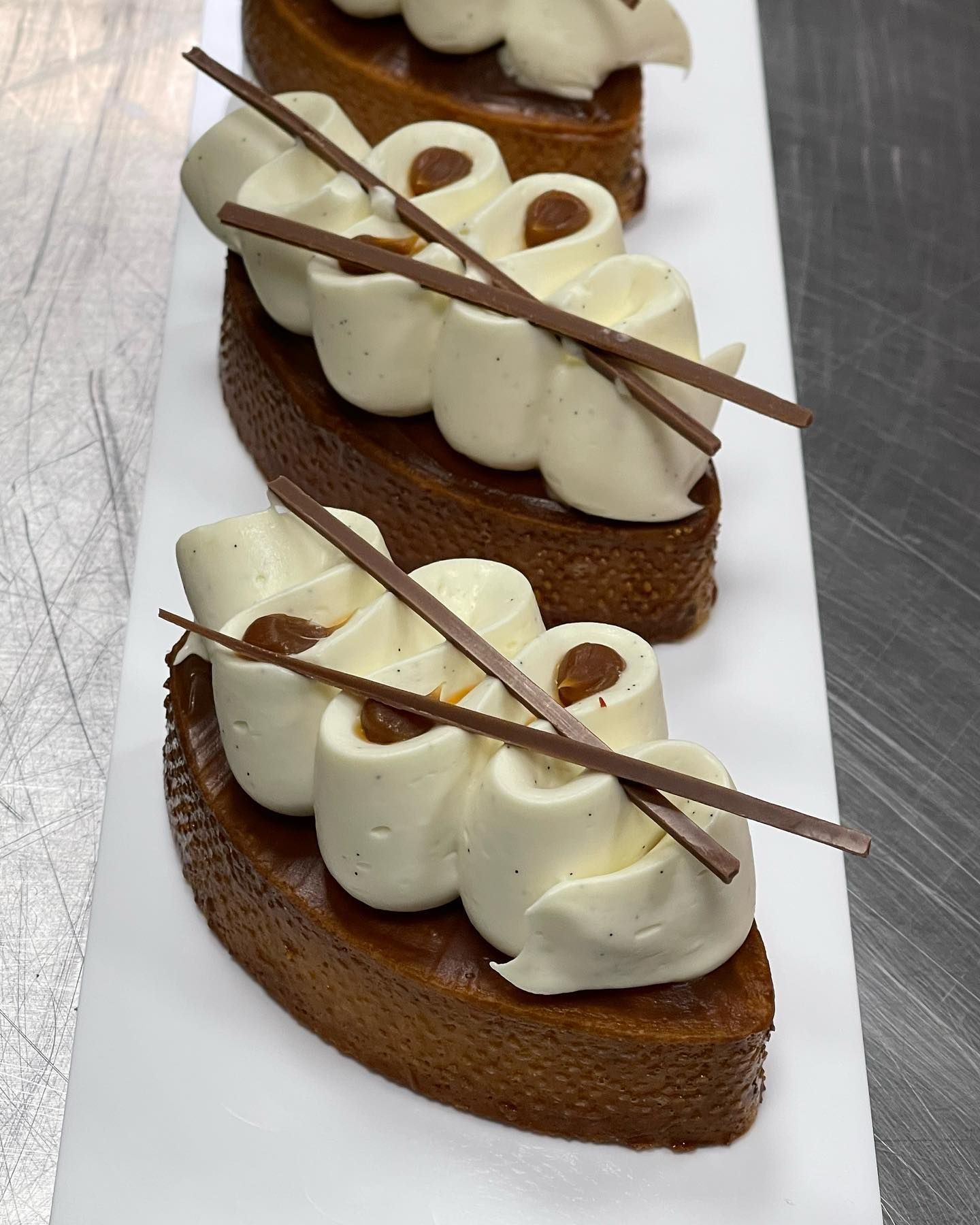 Mini crostatine al caramello guarnite con panna montata e bastoncini di cioccolato su un piatto bianco.