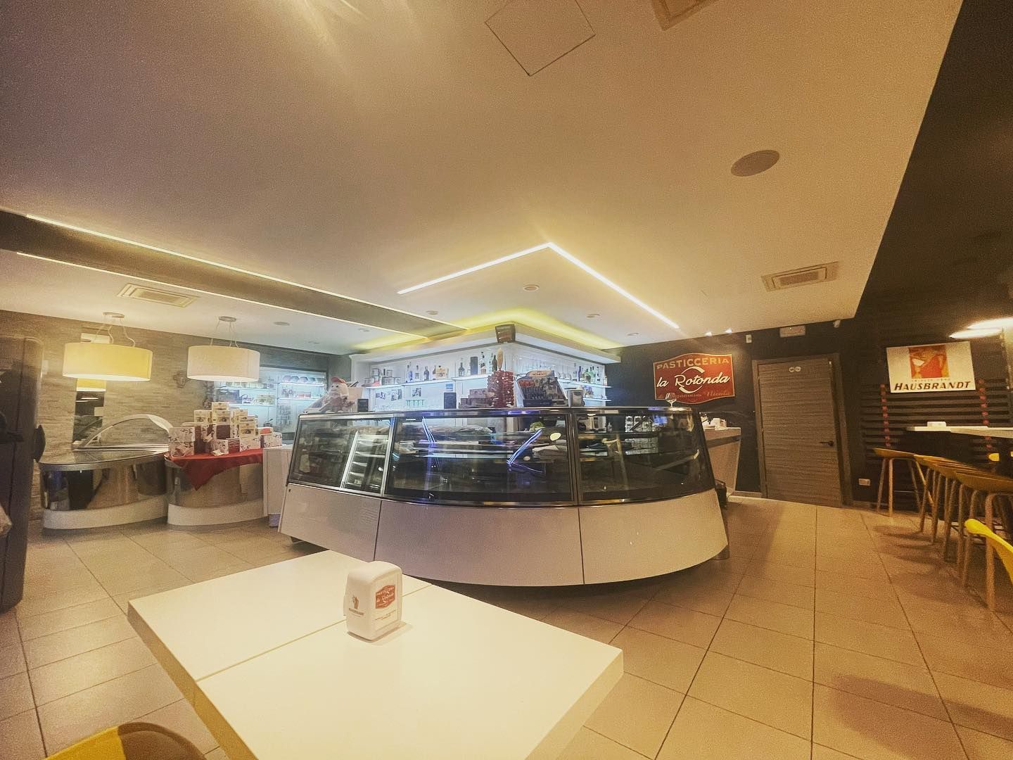 Interno di un bar con una vetrina di dolci e alcuni tavoli.