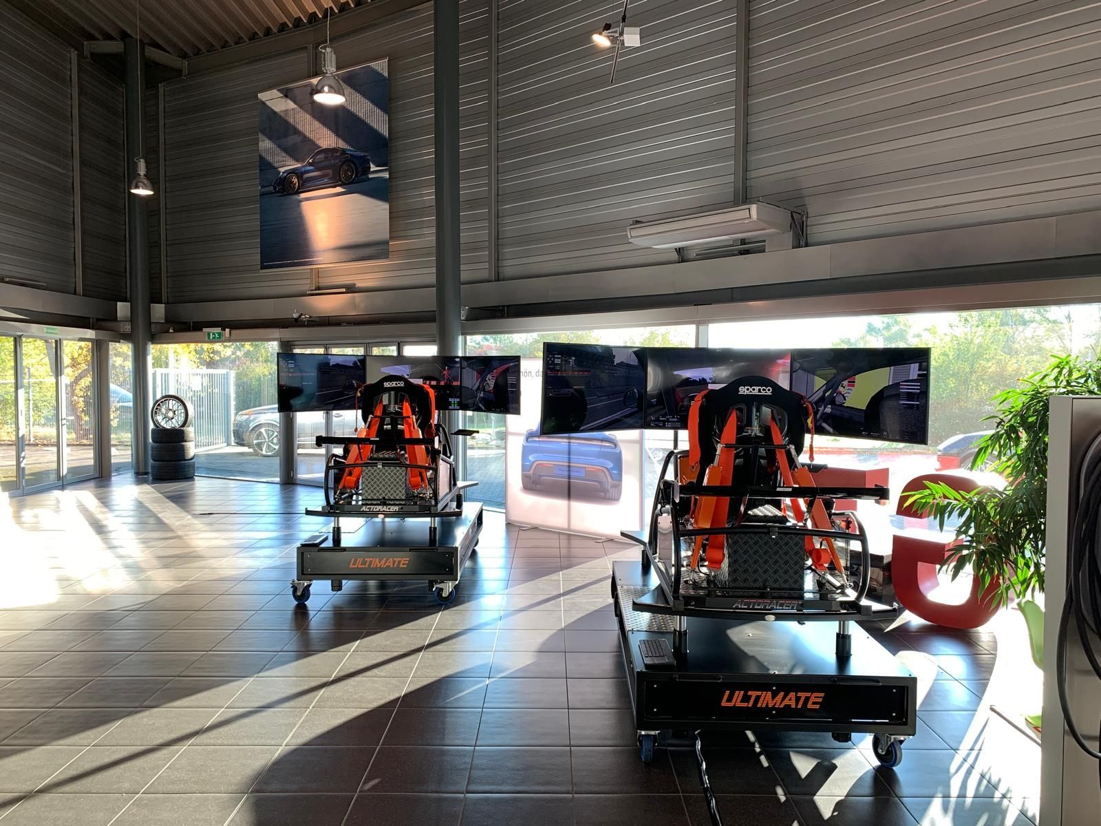 Zwei orangefarbene Rennwagen sind in einem hellen Ausstellungsraum mit Glaswänden und poliertem Fliesenboden zu sehen.