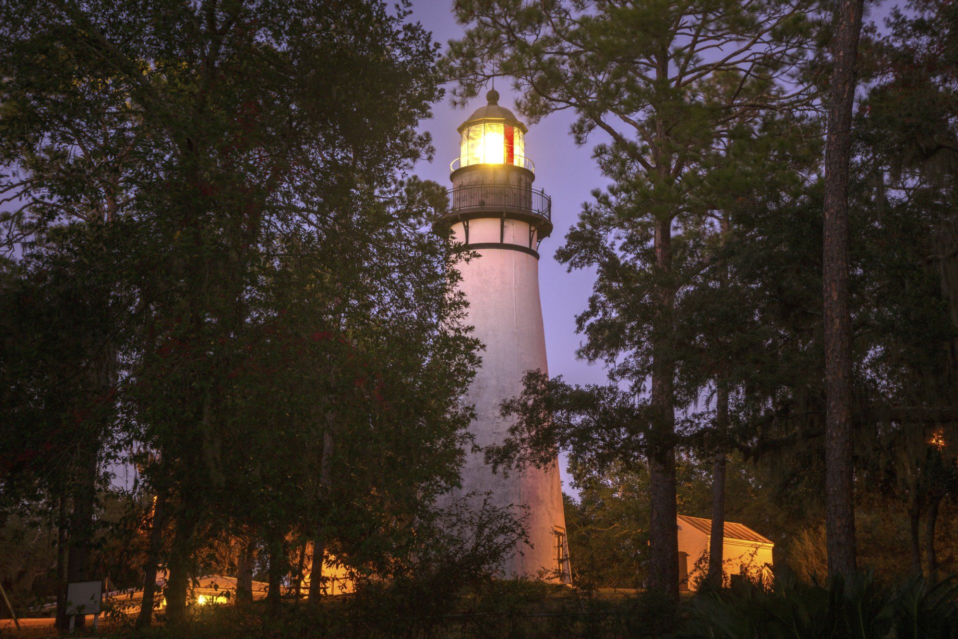 a lighthouse is lit up at night surrounded by trees