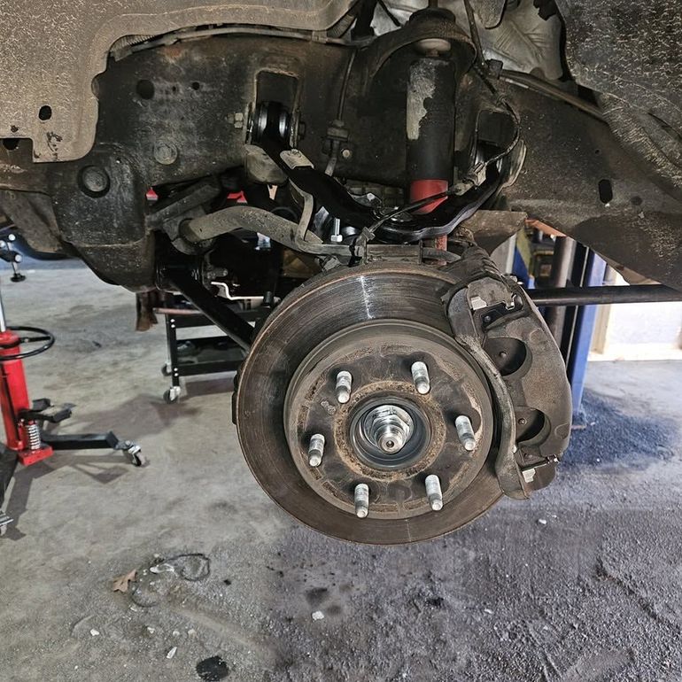 Car wheel and brake assembly exposed in a garage, with the vehicle lifted on a jack.