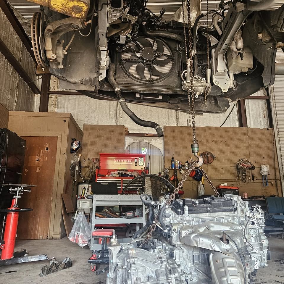 Auto repair shop with car underside lifted overhead and two transmission engines on the floor below