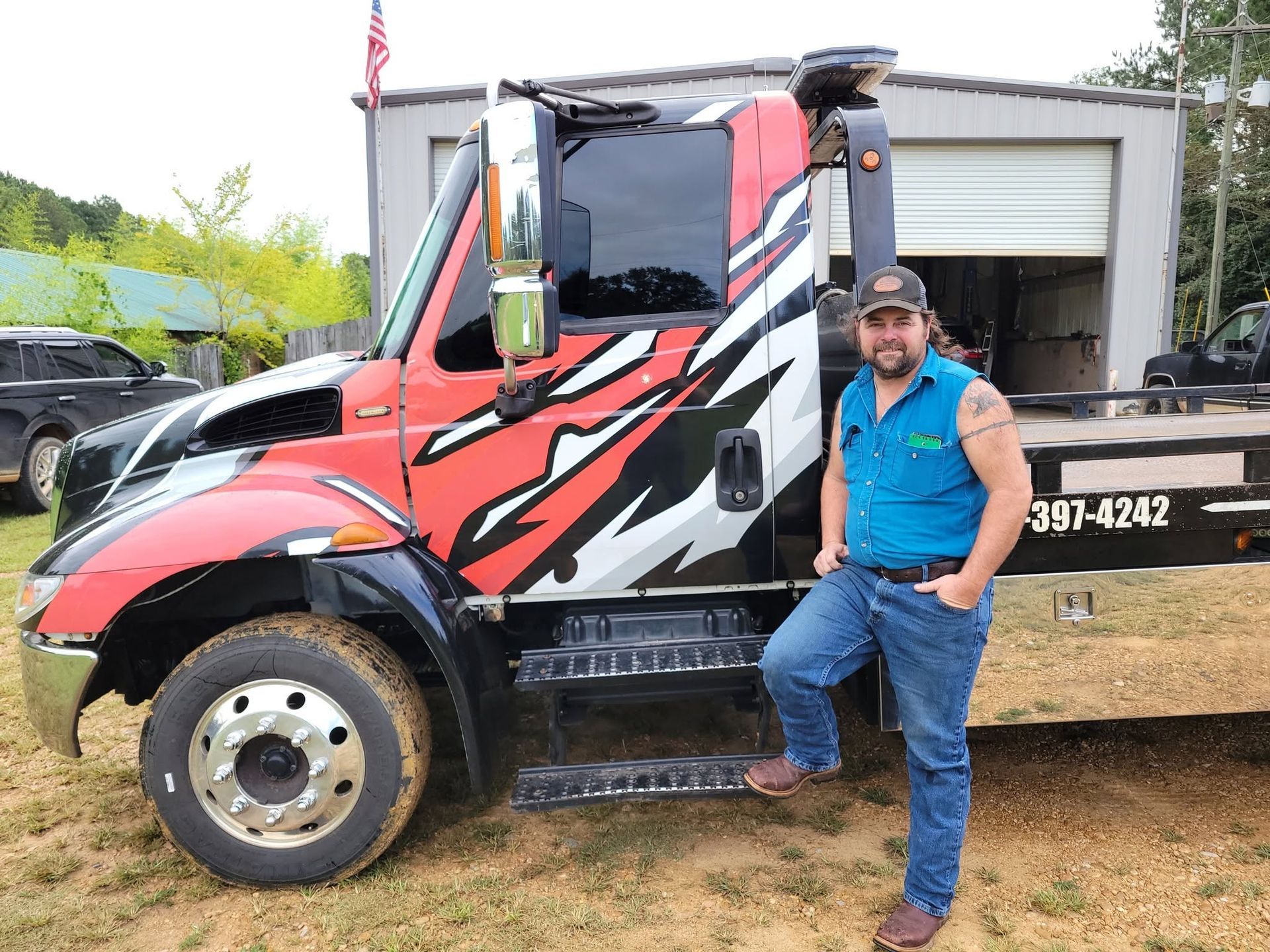 Man leaning on a red and black truck at a worksite with a gravel bed and open trailer