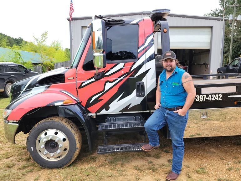 Man standing beside a red-and-black dump truck at a muddy worksite