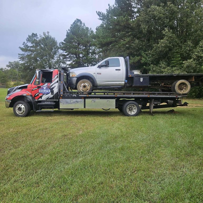 Tow truck hauling a silver pickup truck on a flatbed in a grassy field.