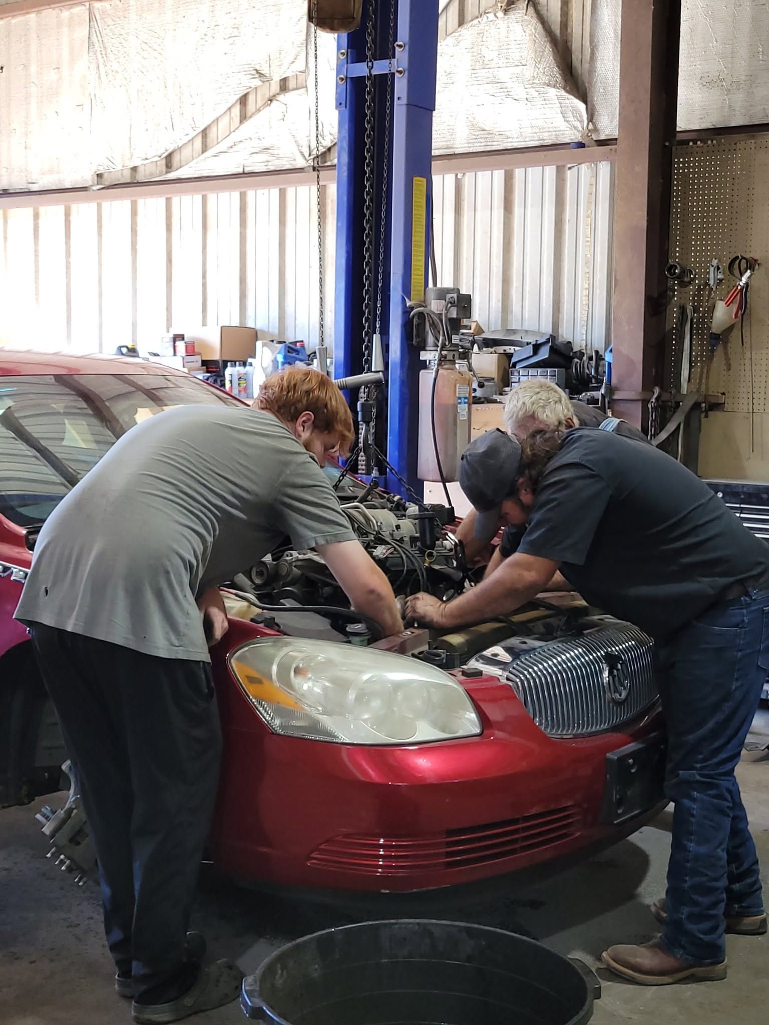 Two mechanics working under the hood of a red car in a repair shop