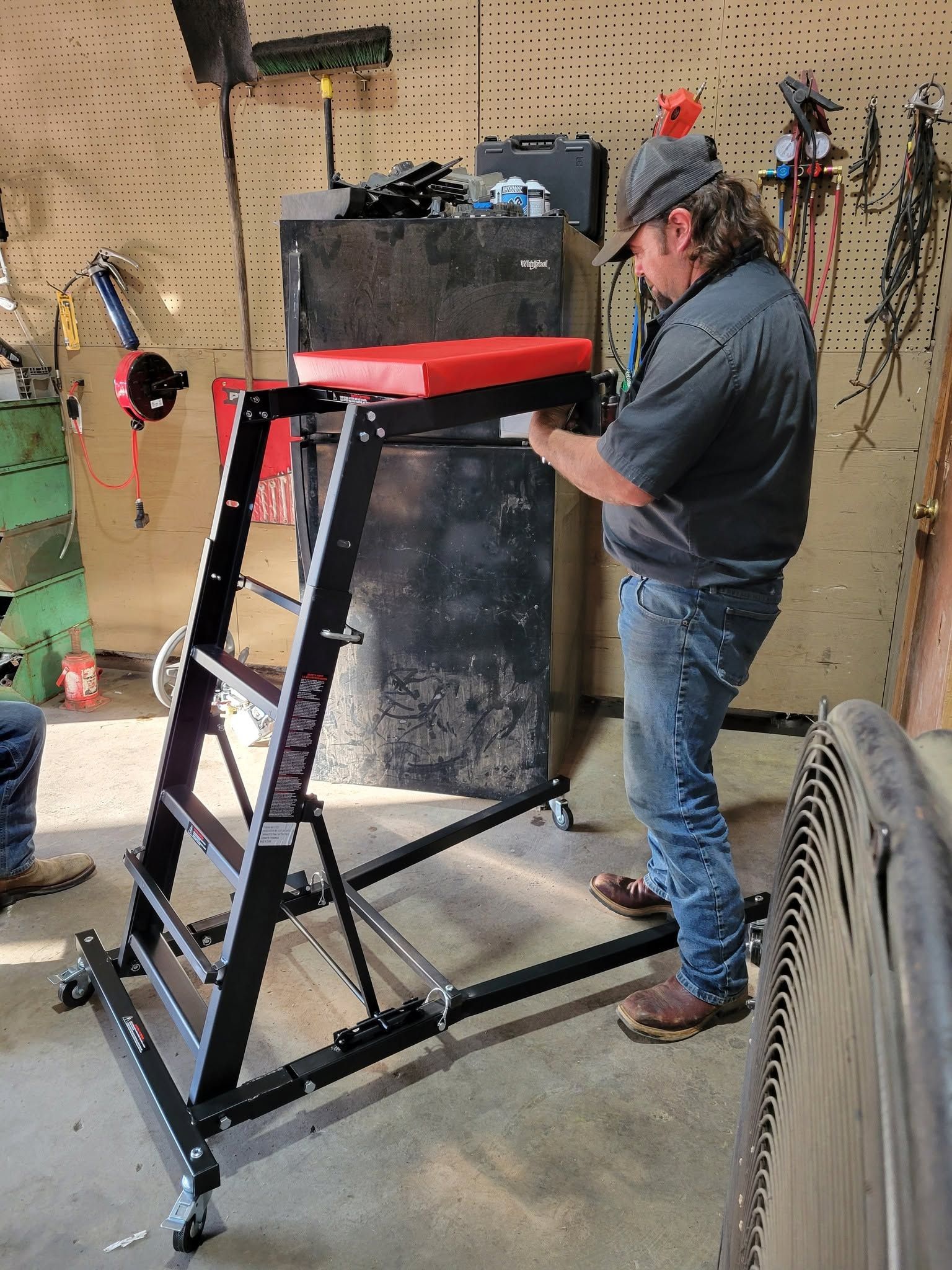 Person adjusting a black metal stand with a red top in a workshop garage