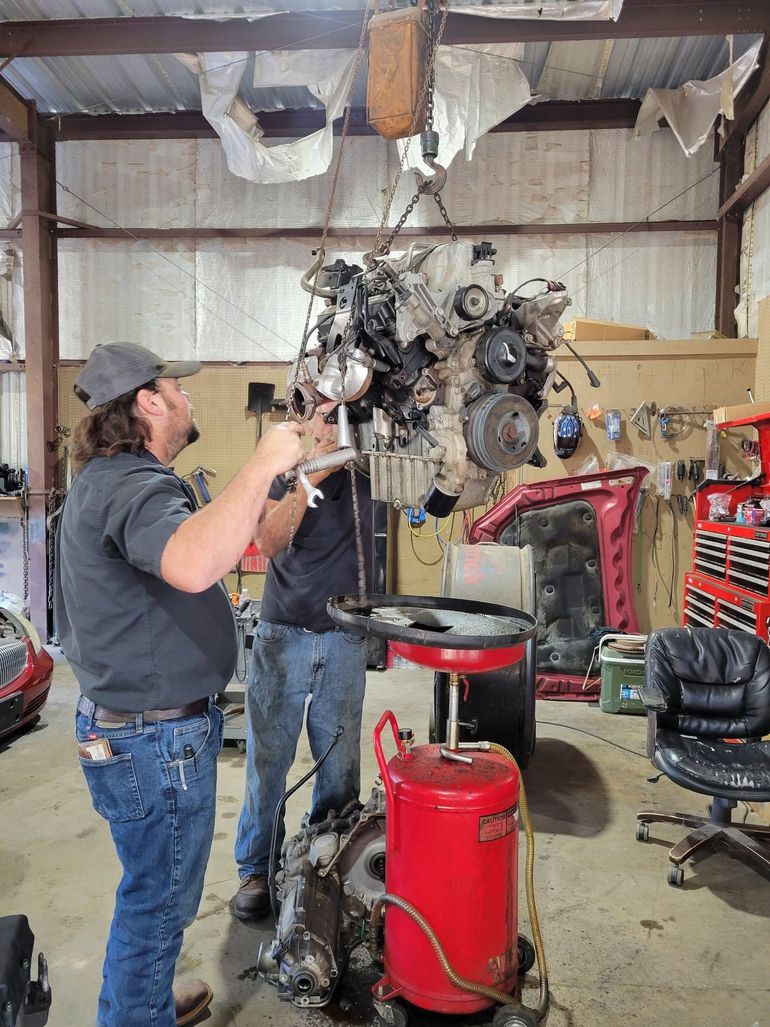 Mechanic working on a suspended engine in a garage workshop beside a red tool chest