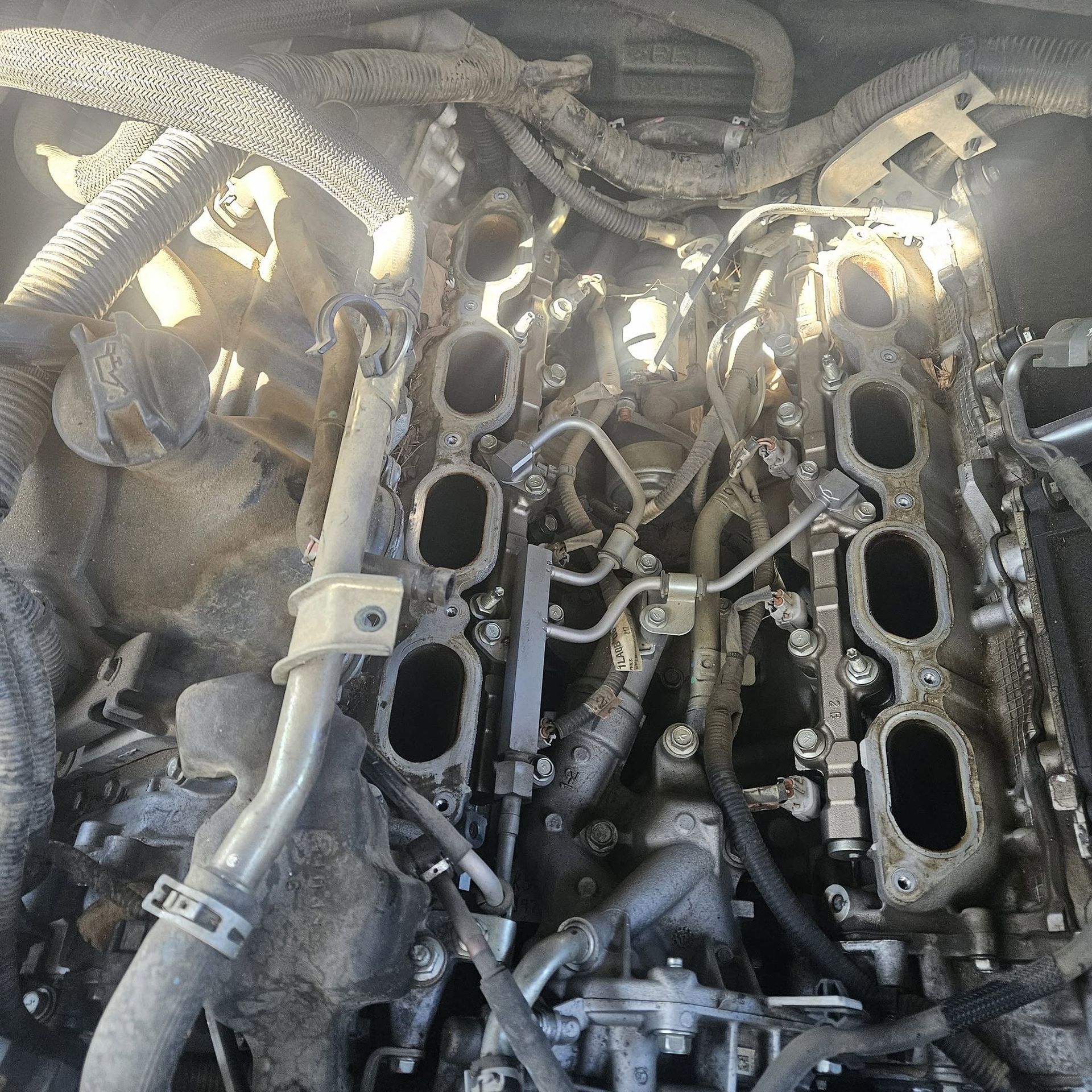 Close-up of a dusty car engine with the intake manifold removed, exposing open cylinder ports and hoses.