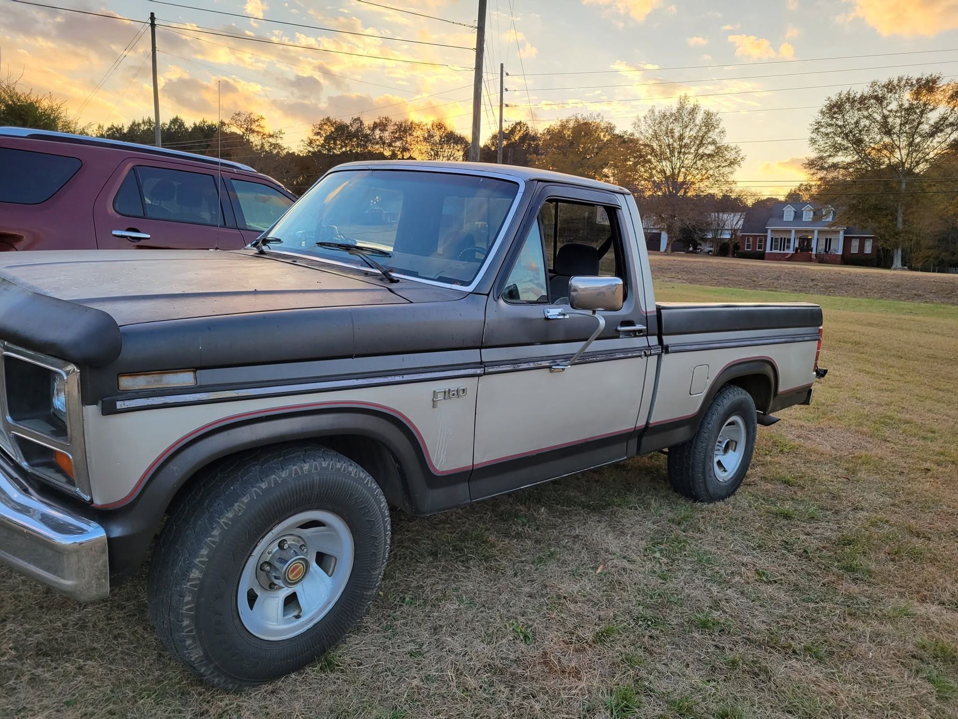 Beige vintage pickup truck parked on grass at sunset, with another vehicle behind it.