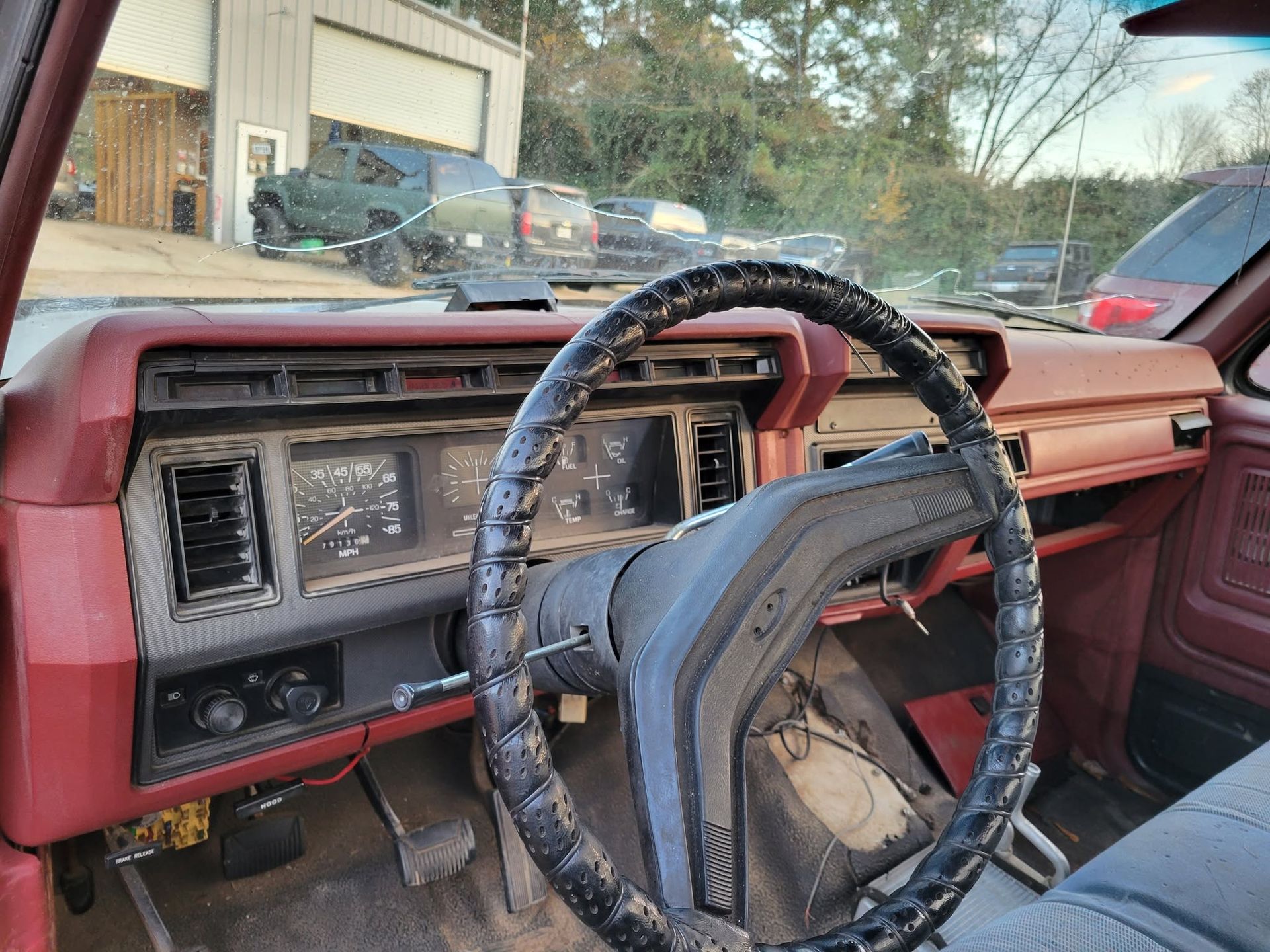Old maroon car interior with worn dashboard, steering wheel, and windshield view of a garage