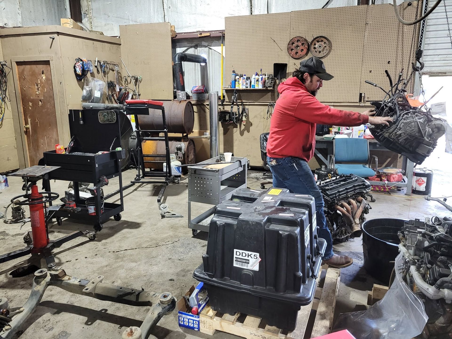 Person in a red hoodie working in a cluttered workshop beside machinery and buckets