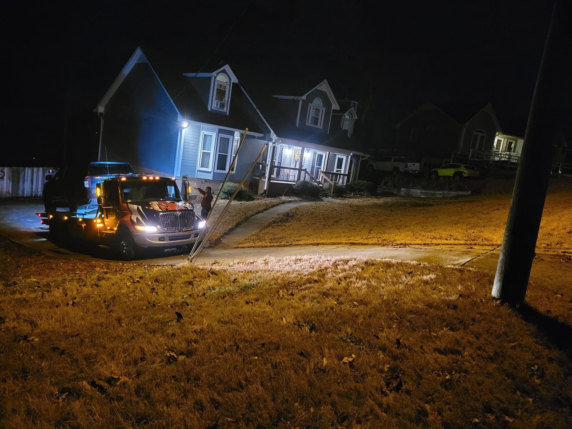 Police SUV with flashing lights parked on a wet street at night beside a lit house