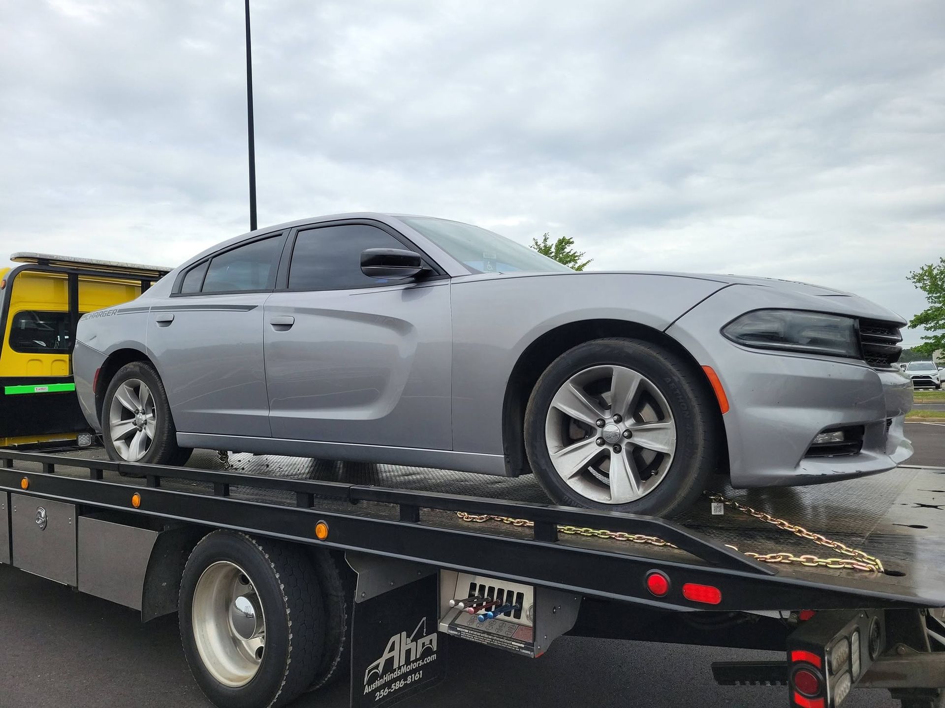 Gray Dodge Charger on a flatbed tow truck, seen from the side outdoors.