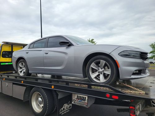Gray Dodge Charger on a flatbed tow truck outdoors under a cloudy sky