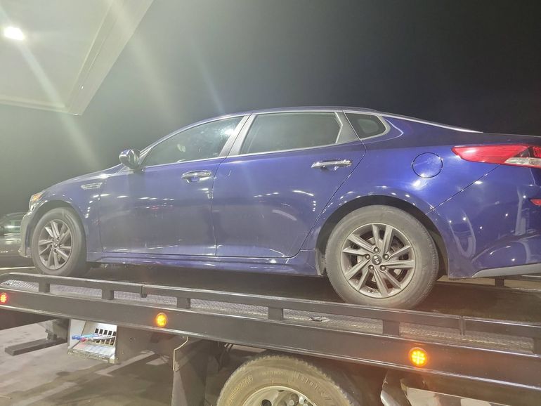 Blue sedan on a tow truck at night with lights on