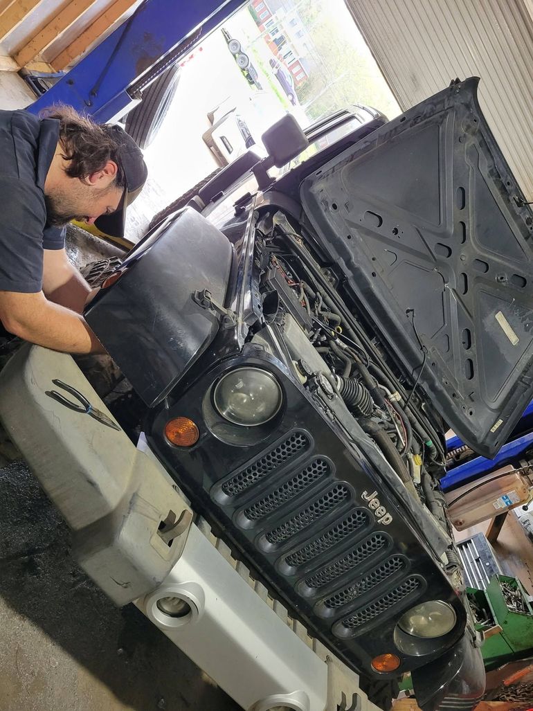 Mechanic working on a lifted black SUV with its hood open in a garage