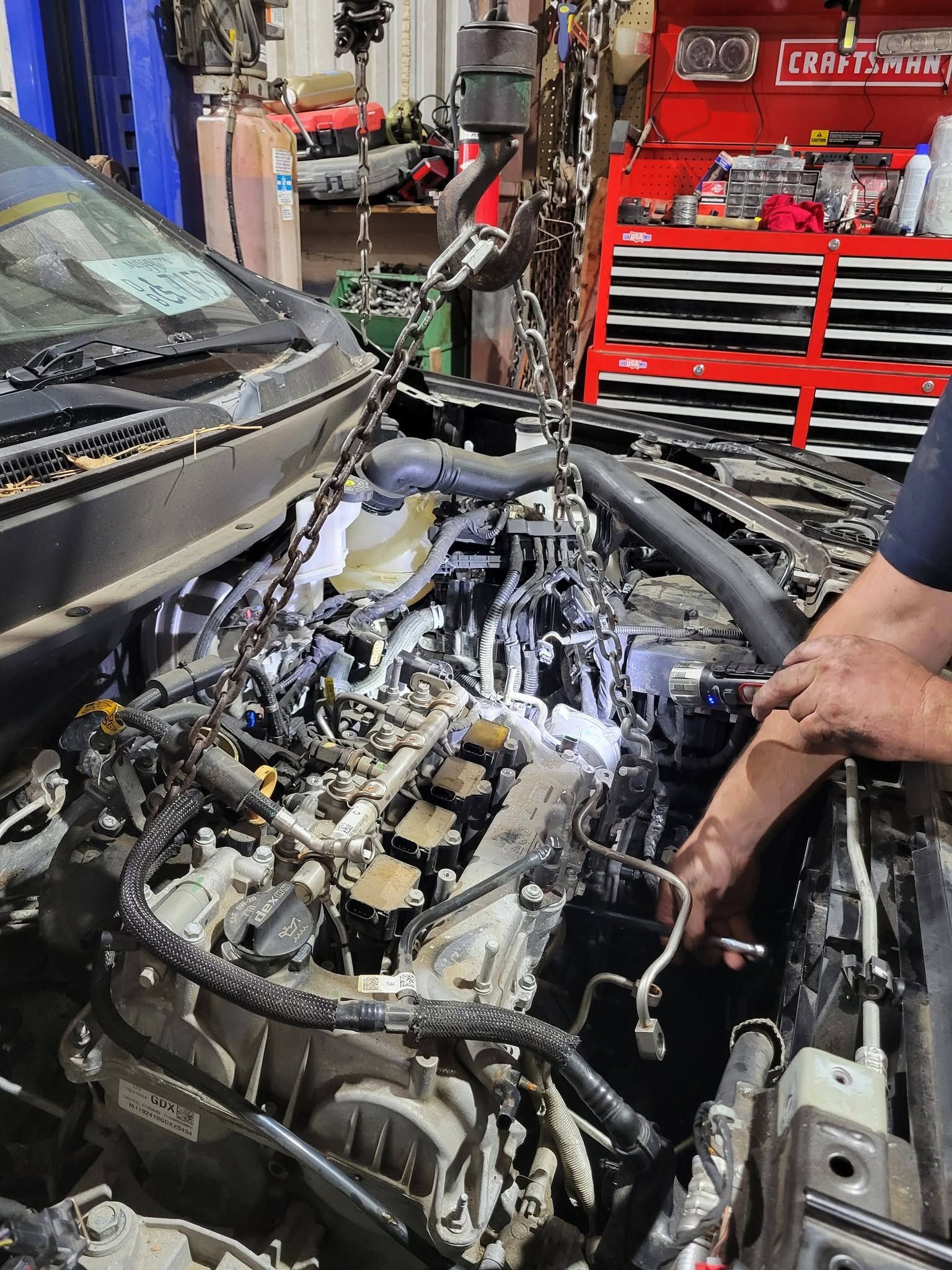 Damaged car engine bay with severe fire damage, open hood, and a person inspecting it in a repair shop
