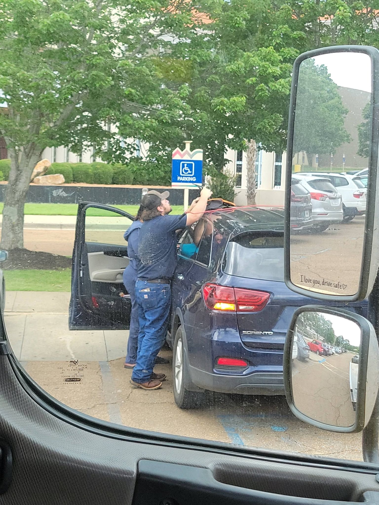 Person loading a blue sedan at a curbside pickup spot, seen from inside another vehicle.
