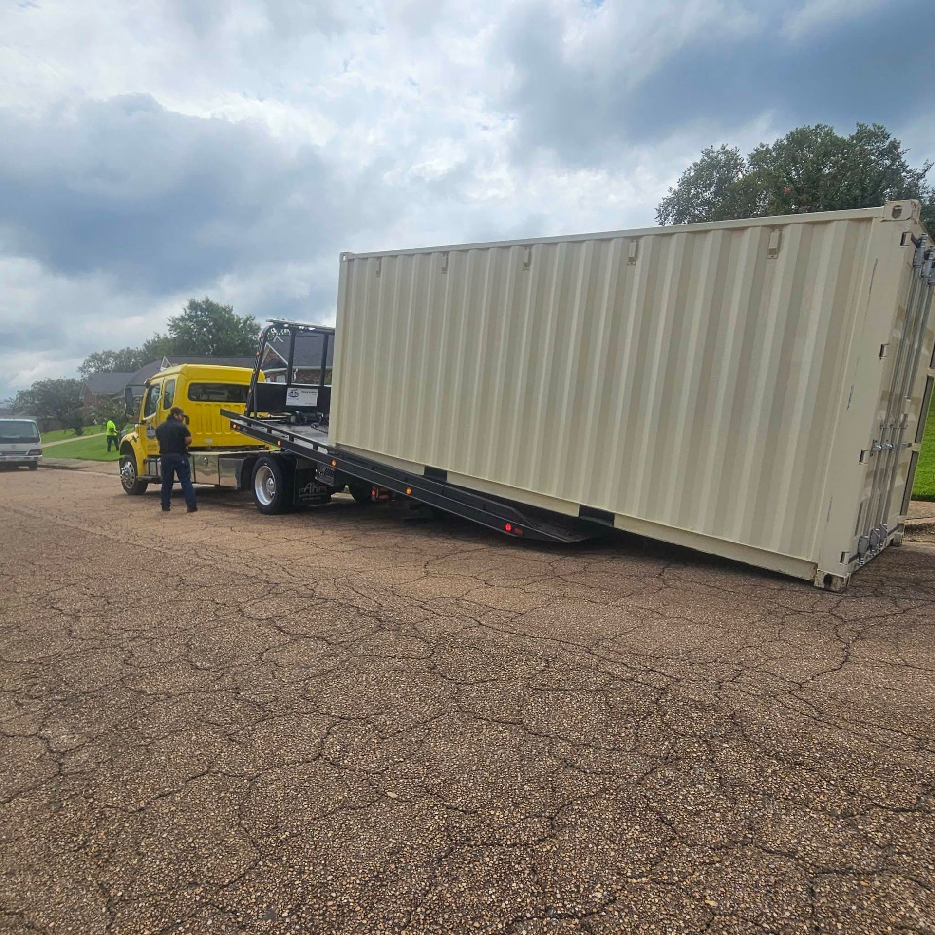 Tow truck lifting a tipped white shipping container on a gravel lot under cloudy skies