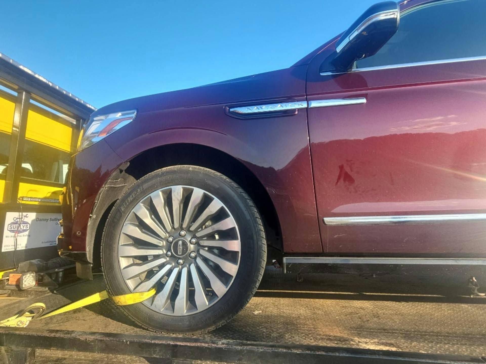 Maroon SUV on a tow truck with a wheel strap, viewed from the front side.