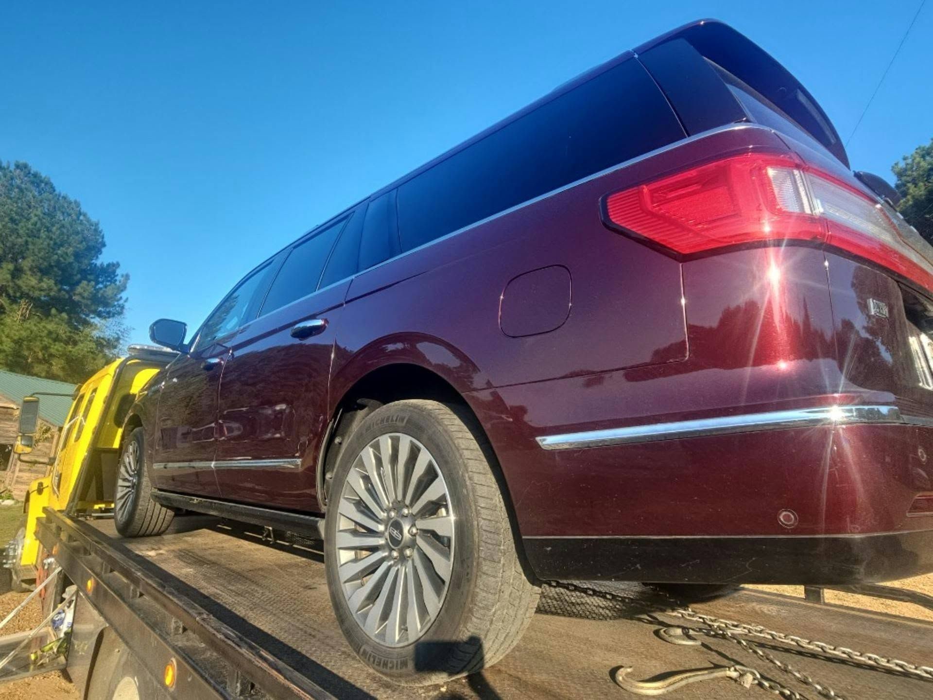 Maroon SUV loaded on a tow truck under a blue sky