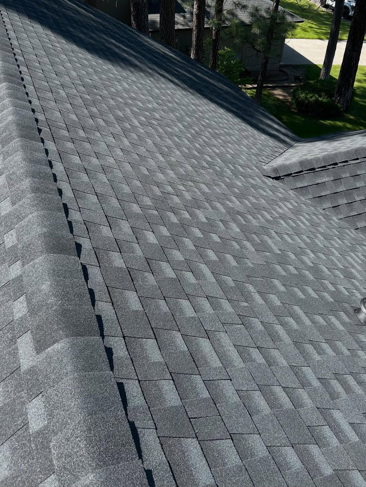 A high-angle view of a grey, asphalt-shingled residential roof with a visible hip and valley section.