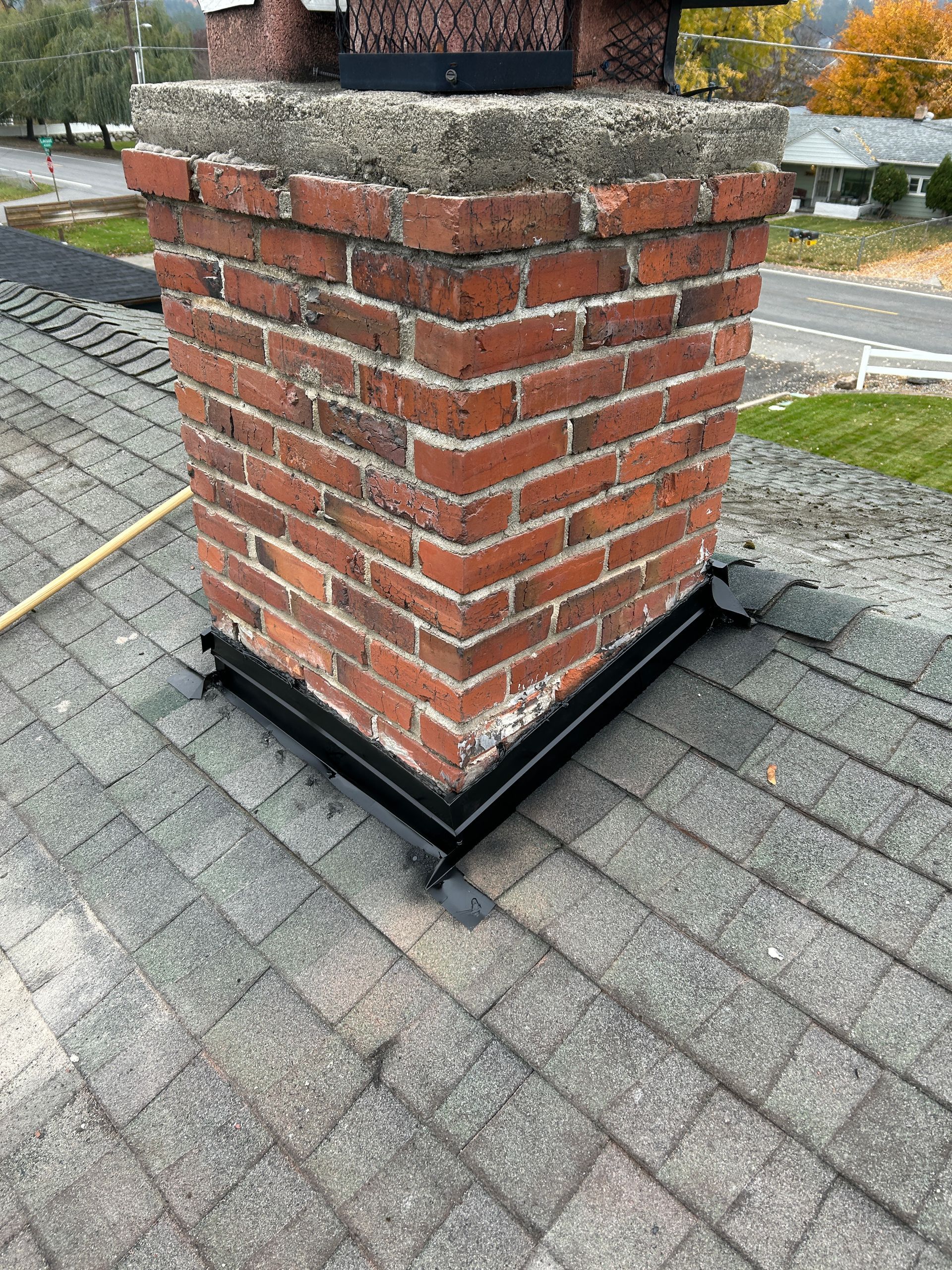 A brick chimney on a shingled roof with black flashing installed around its base.