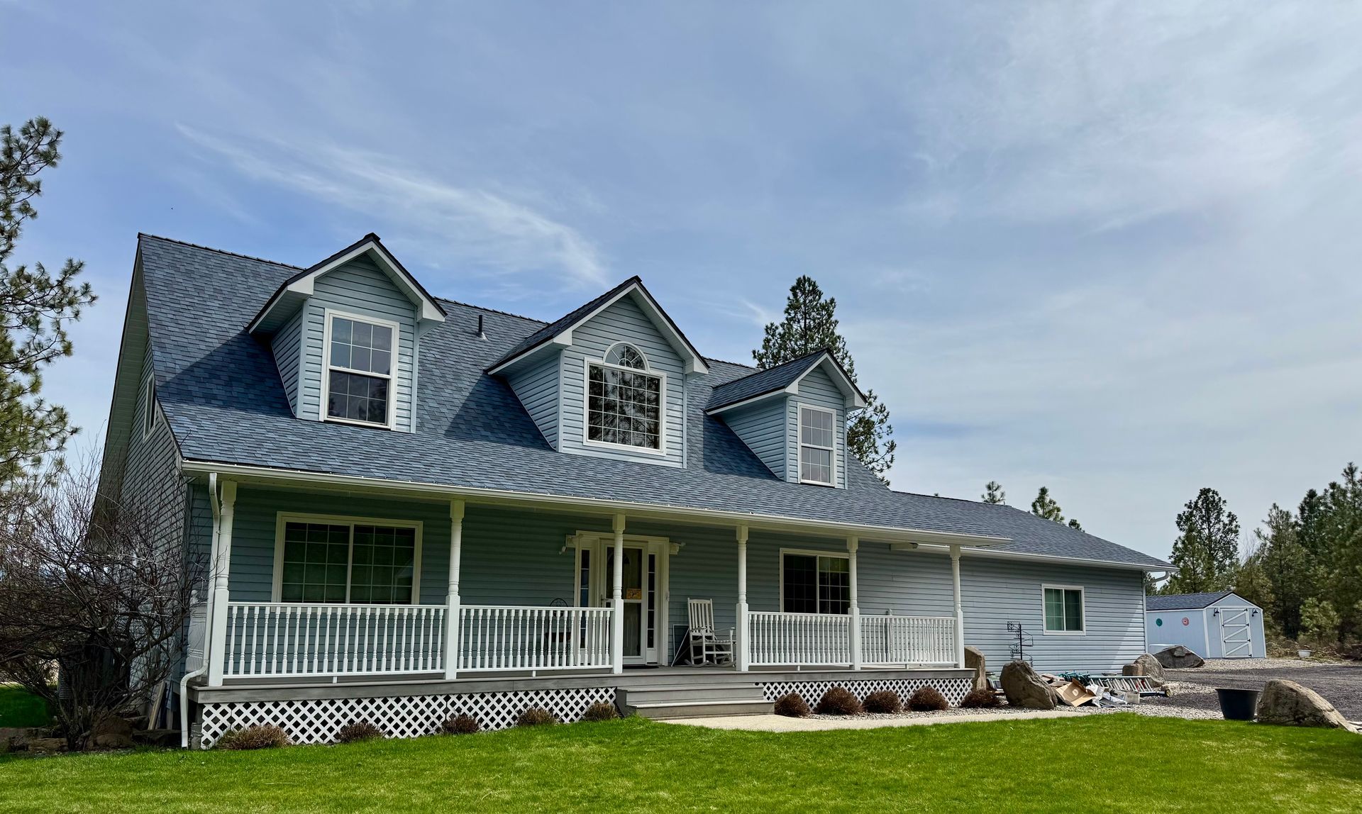 Light blue house with a covered front porch, white railings, and three dormer windows under a blue roof.