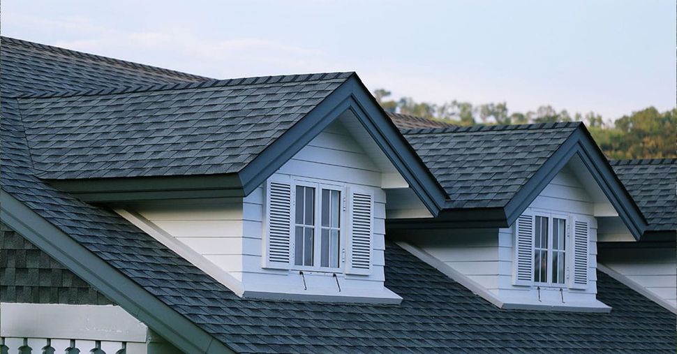 Two roof dormers with white-trimmed windows and blue-grey shingled roofs set against a light sky.