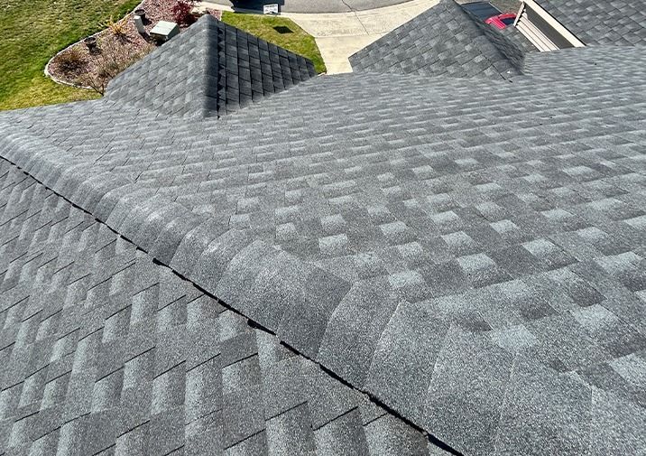 A high-angle view of a grey, asphalt-shingled residential roof with multiple peaks and a hip section.