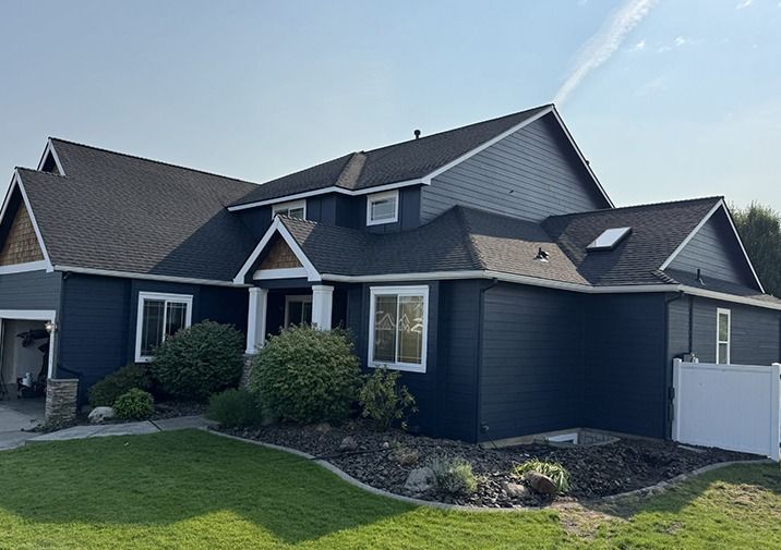 Dark blue suburban house with a gray roof, white trim, and a green lawn on a sunny day