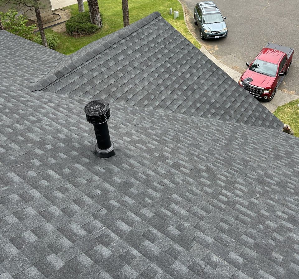 High-angle view of a grey shingled roof with a black plumbing vent, overlooking a driveway with two parked cars.
