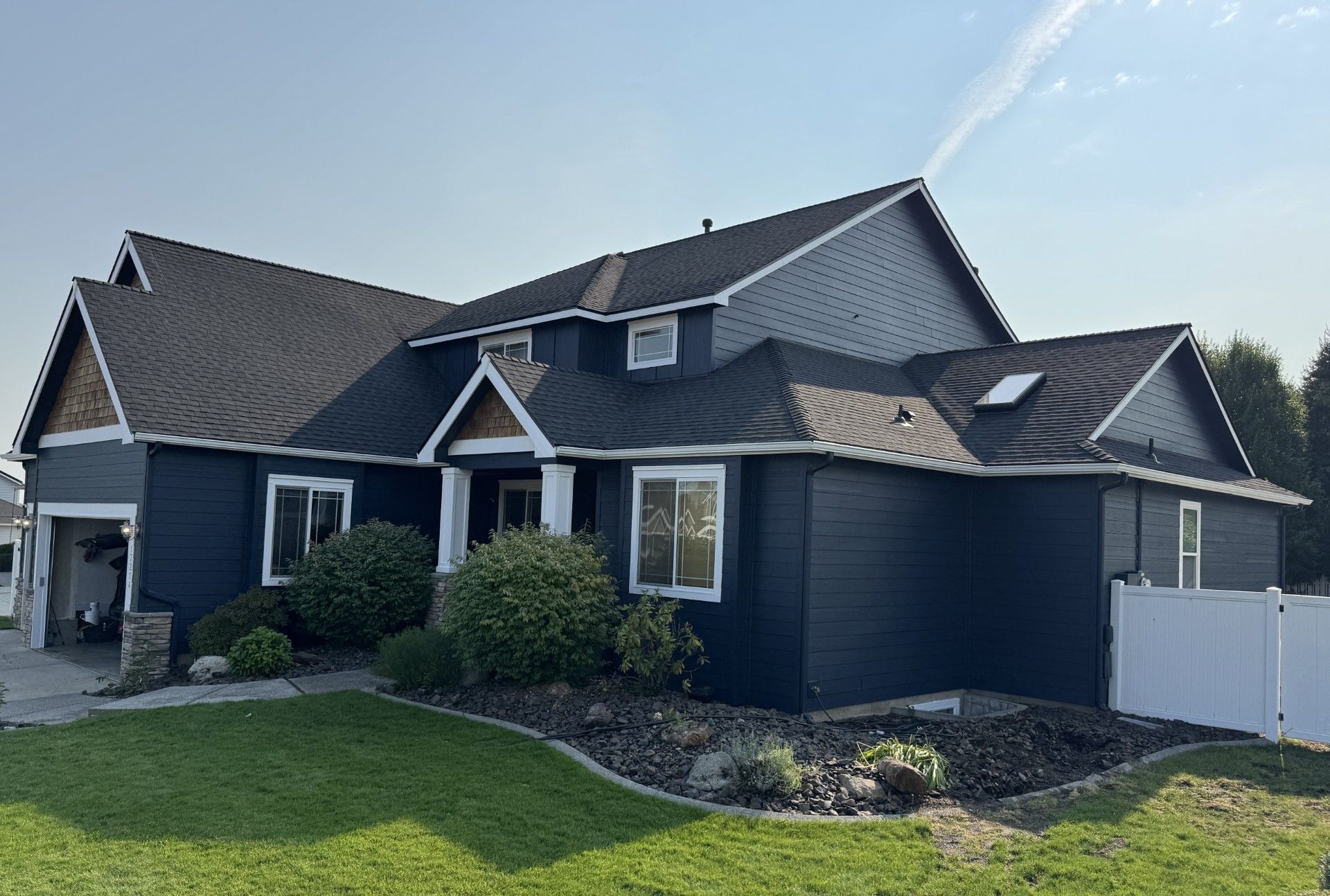 Dark blue two-story suburban house with a gray shingled roof, white trim, and a green front lawn on a sunny day.