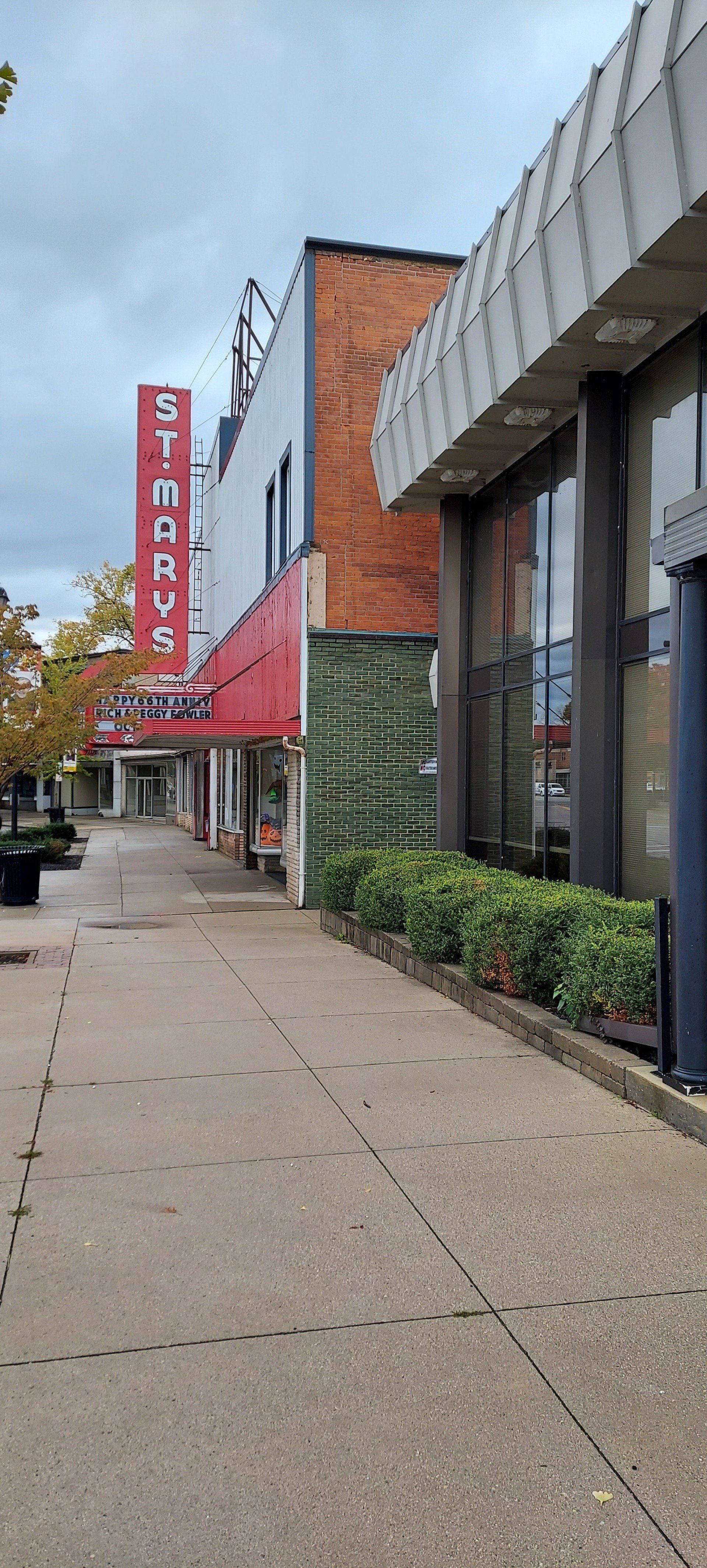 A sidewalk leading to a building with a red sign on it.
