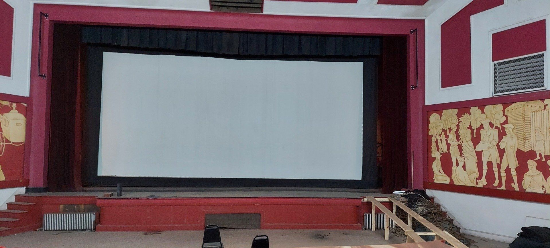 An empty stage with a red curtain and a white screen.
