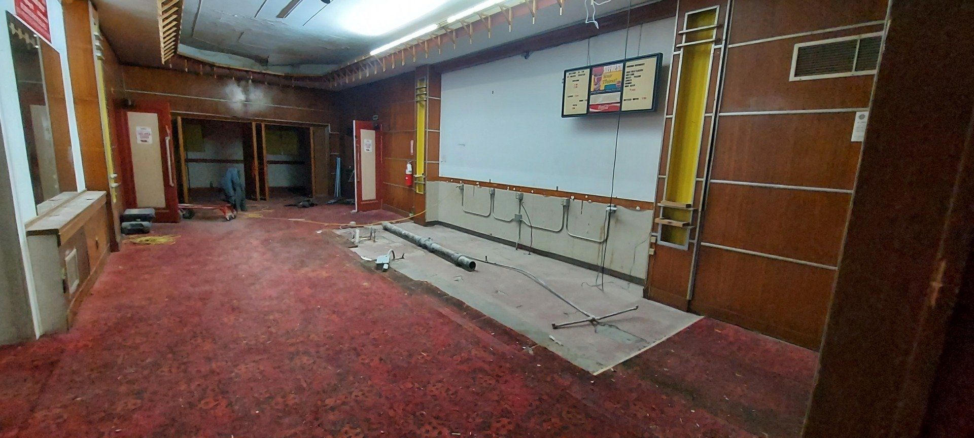 An empty room with a red carpet and a television on the wall.