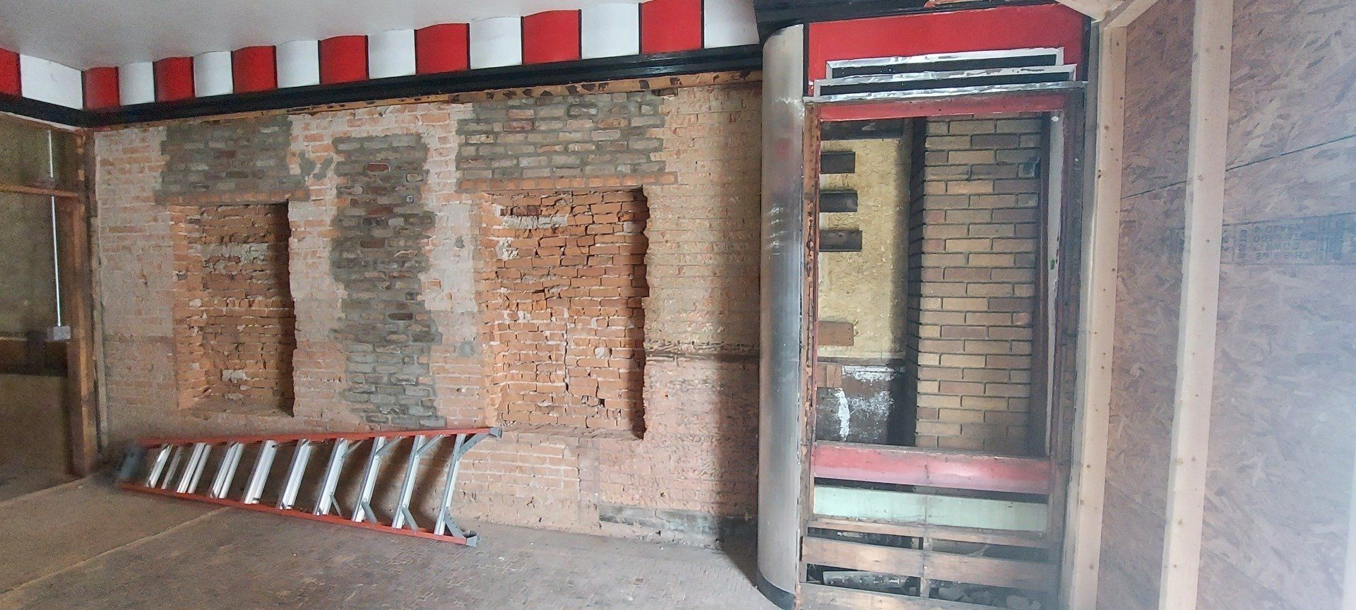 An empty room with a ladder and a brick wall.