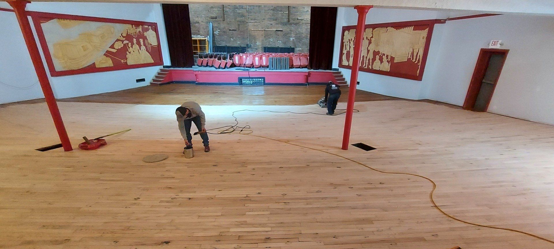 A man is working on a wooden floor in a large room.